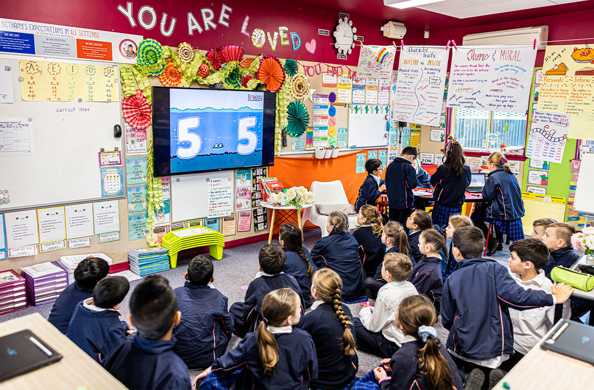 Students sitting together on the classroom floor watching a screen at Bethany Catholic Primary School Glenmore Park